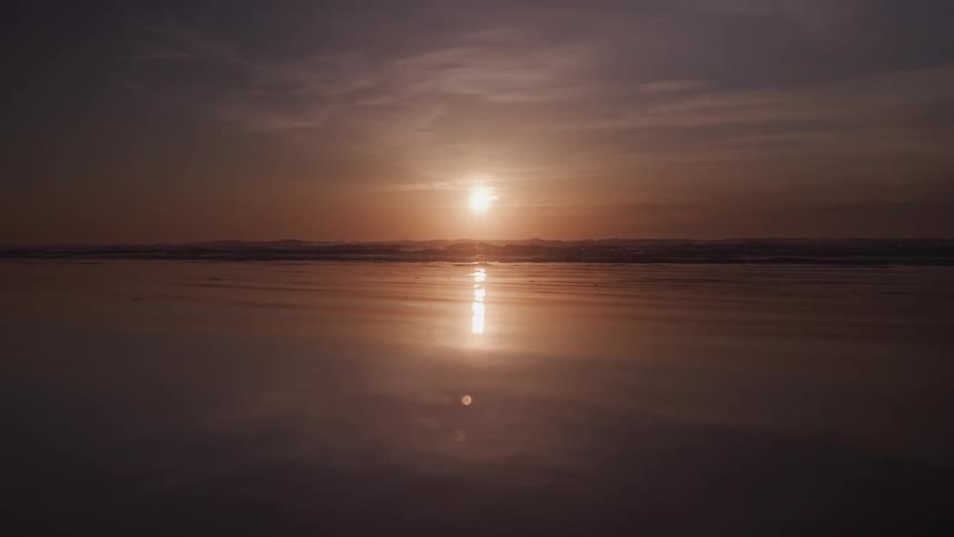 A serene beach scene at dusk with the suns reflection creating a shimmering path across the wet sand