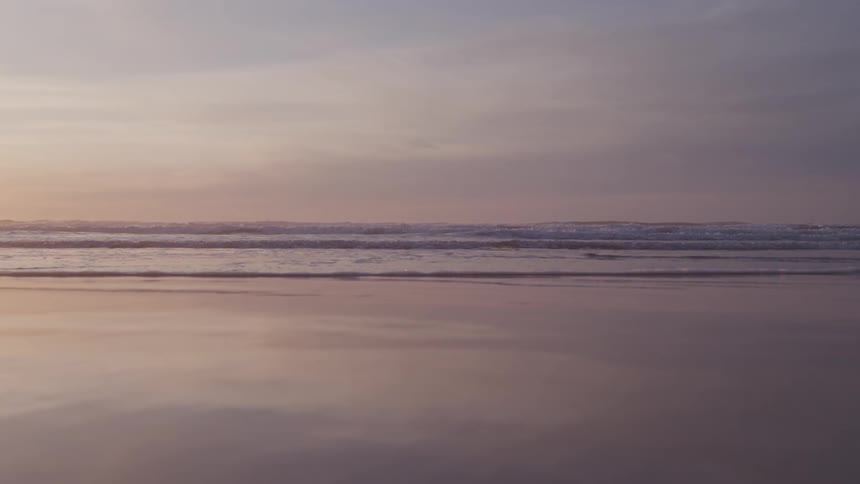 A serene beach scene captures the calm of sunset with waves gently rolling onto the wet sand