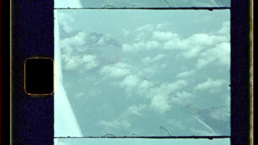 Looking out from within an aircraft a vast expanse of fluffy white clouds stretches to meet the horizon partially obscured by the airplanes wing all framed by the distinctive border of an analog film strip