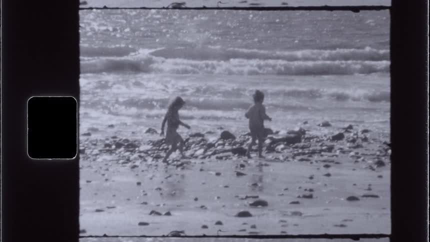 A boy and girl walk along a rocky sandy beach