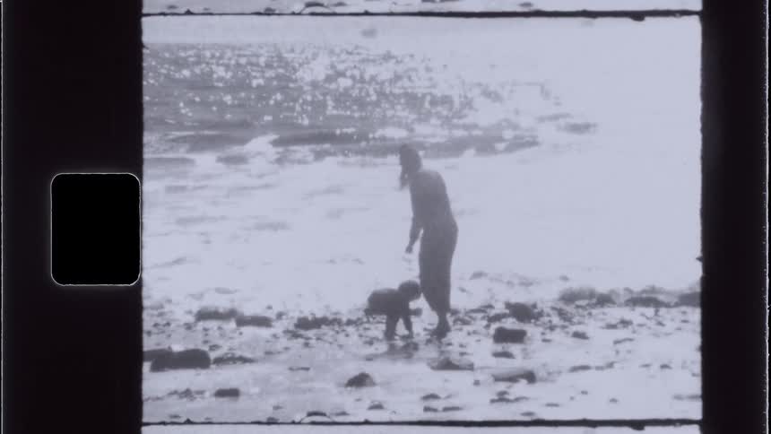 A child picks up a rock on the beach