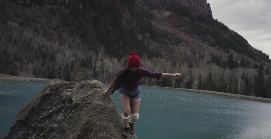 A woman jumps off a rock near a mountain lake