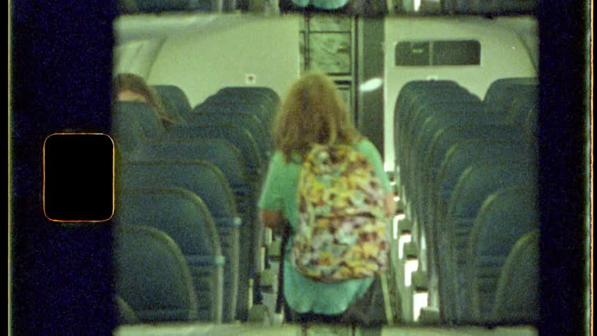 A child from behind wearing a colorful backpack with yellow details walking in the aisle of a bus with several free seats