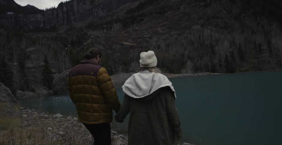 Man and woman hold hands and walk towards a lake