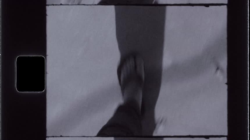 A person wearing sandals walking over a sandy terrain captured on vintage film