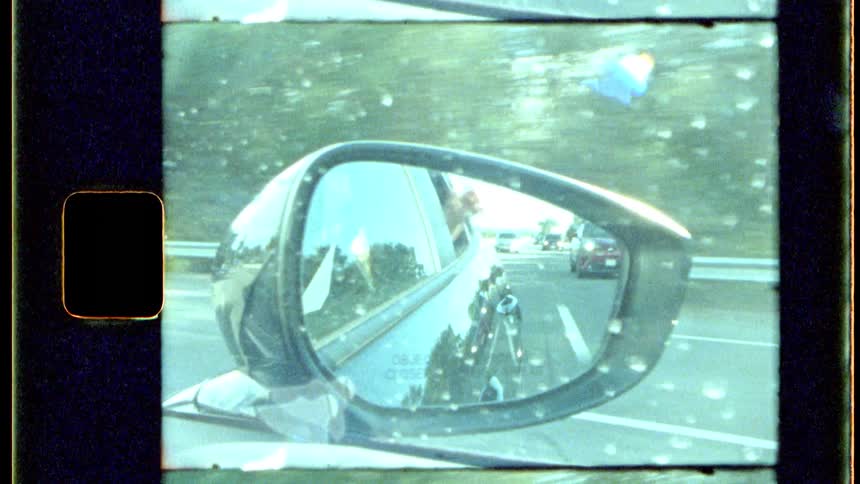 Side mirror reflects a passenger waving out the car window during a summer drive
