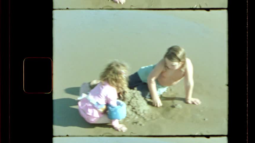 A little boy and a little girl are lying on the edge of a beach playing with a sand castle
