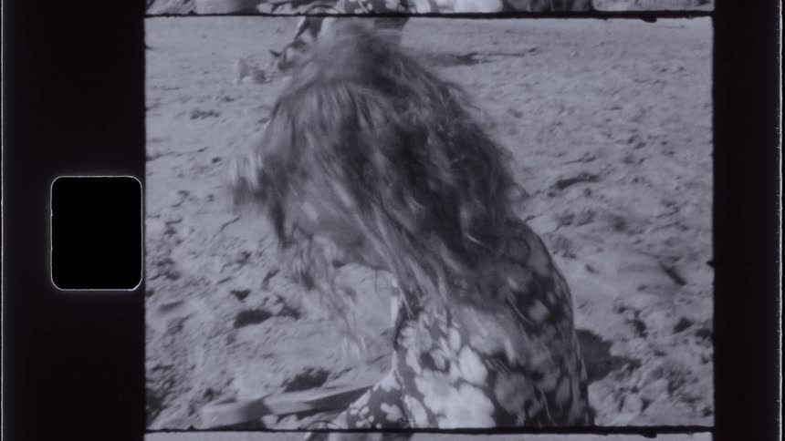 A girl wearing a floral outfit plays in the sand on a beach captured on vintage film