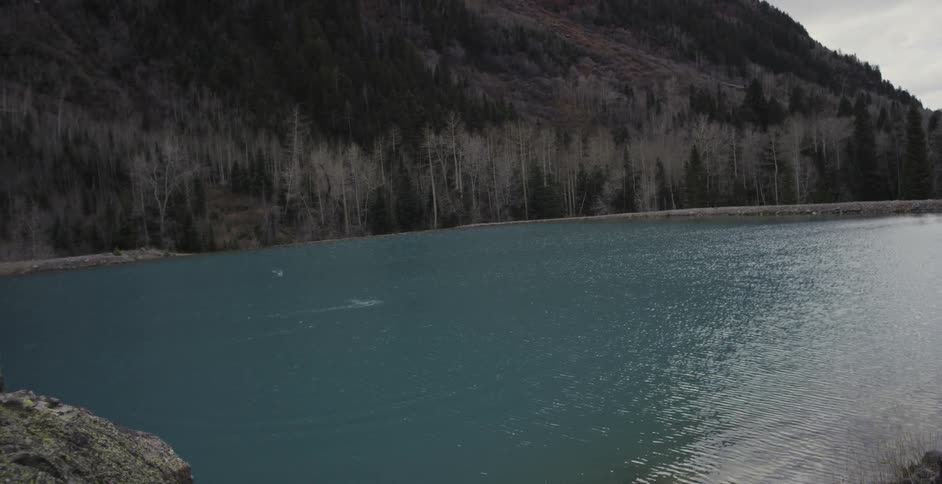 A man skips a rock across a mountain lake
