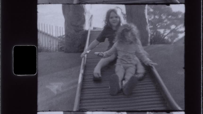 Two young girls are playing on a park slide on a sunny summer day