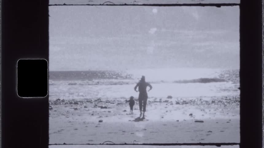 A mother and child walk towards the ocean on the beach