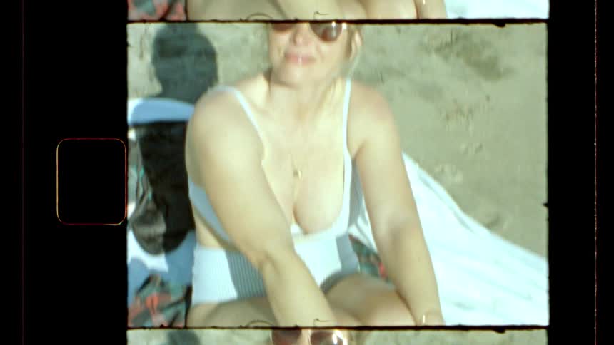 Woman wearing a swimsuit smiles while sitting on a blanket on the beach on a sunny summer day
