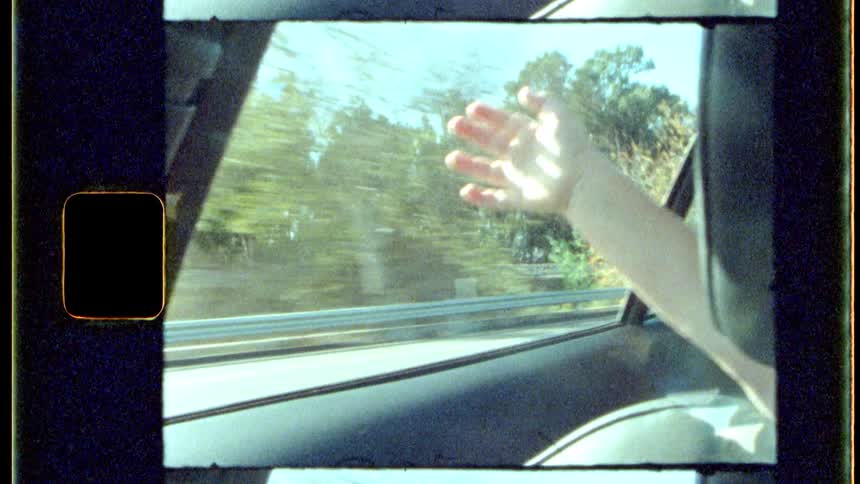 A childs arm with his hand out the window in a fast moving car