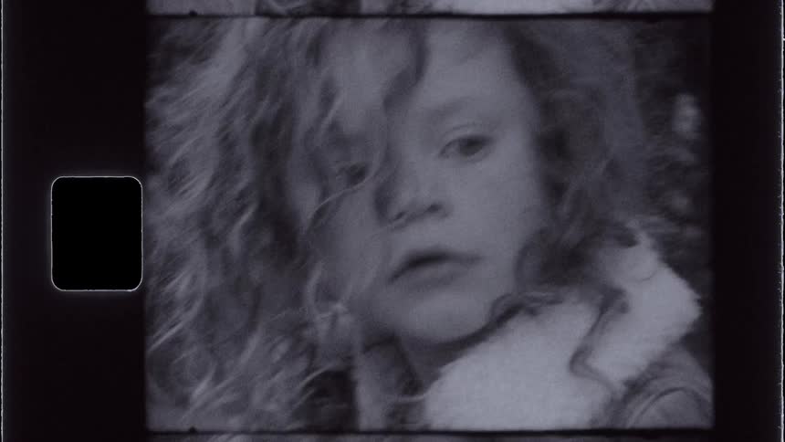 A vintagestyle shot shows a closeup of a girl with curly hair and a lightcolored garment looking around