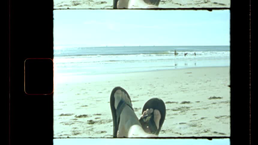 Woman relaxes on the beach while surfers walk through the surf in the distance on a sunny day