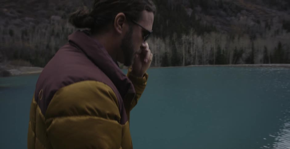 Man in sunglasses picks up a rock to throw into lake