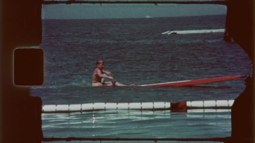 Vintage film with a man paddling in a canoe towards the ocean shore near a peer