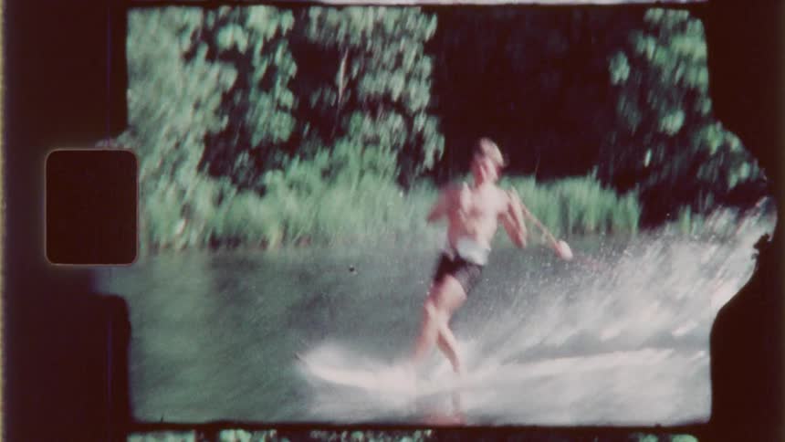 A vintagestyle shot shows a person water skiing on a river with trees lining the background
