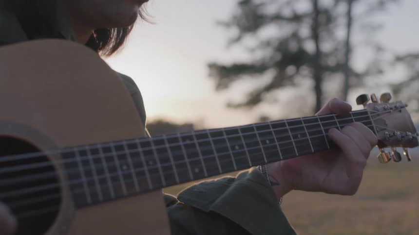 A woman is playing the guitar at sunrise