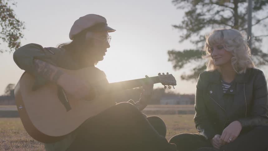 Man sitting next to a woman in a field playing guitar