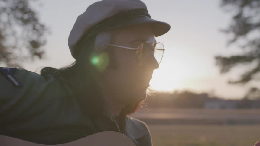 A man wearing a hat is playing guitar and singing