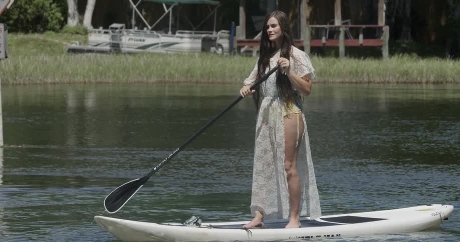 A woman stands and paddles a board in a lake