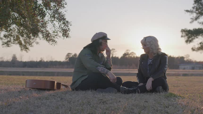 A man and woman sit in the grass with a guitar nearby