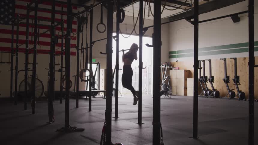 A woman is doing pull ups in the dark gym
