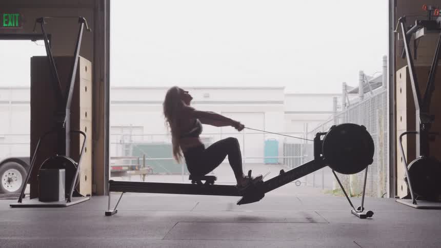 A woman sitting on an exercise machine pulling a rope that is attached to a pulley and going back and forth