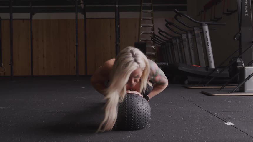 Blonde woman in a gym doing pushups with her hands resting on a ball