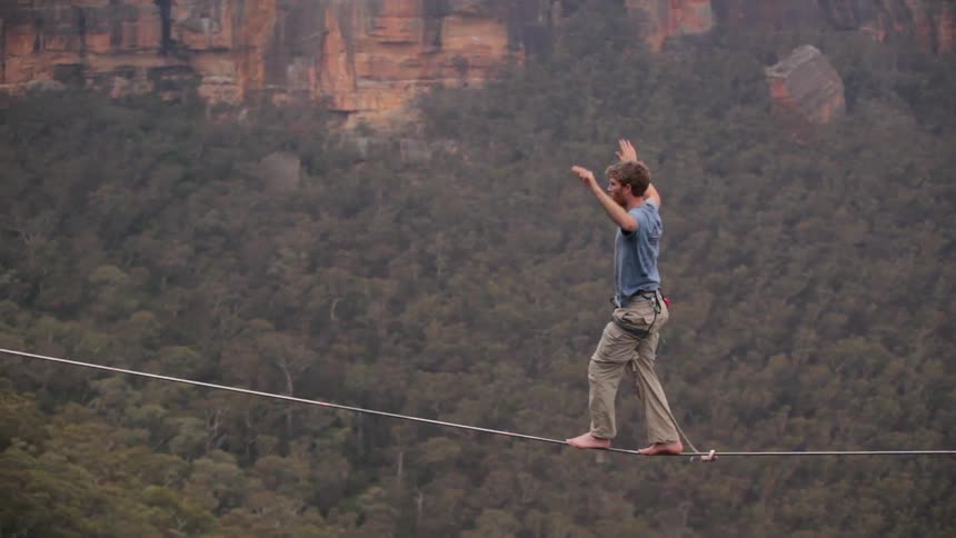 A man crosses a tightrope in a canyon