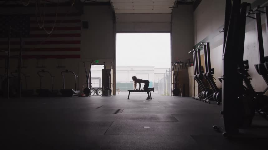 A woman is lifting weights in the dark gym