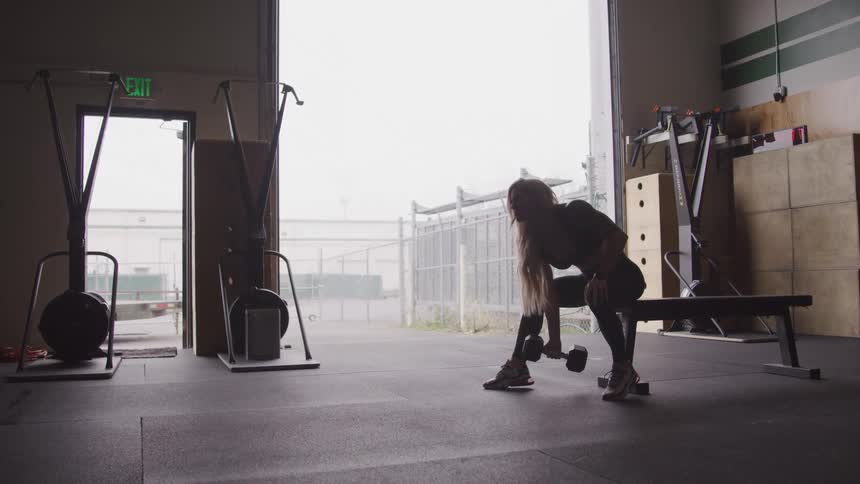 Woman sitting on a bench in the gym training biceps with a dumbbell
