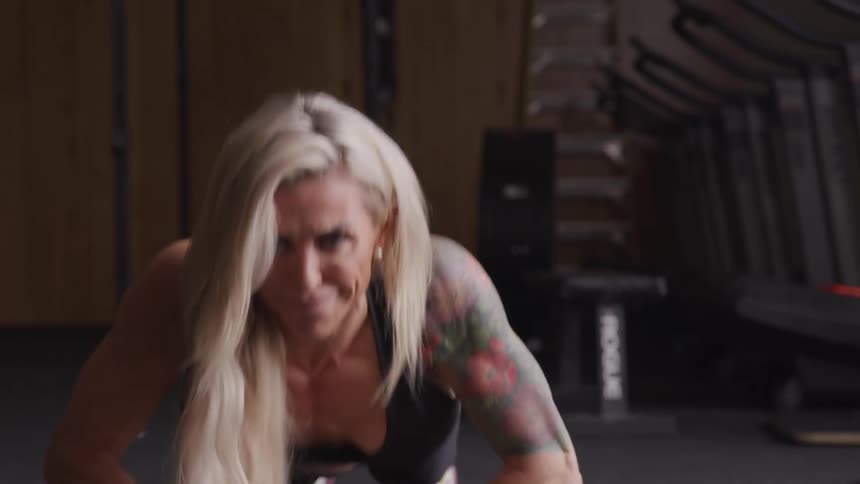 Blonde woman with determined facial expression doing pushups in a gym