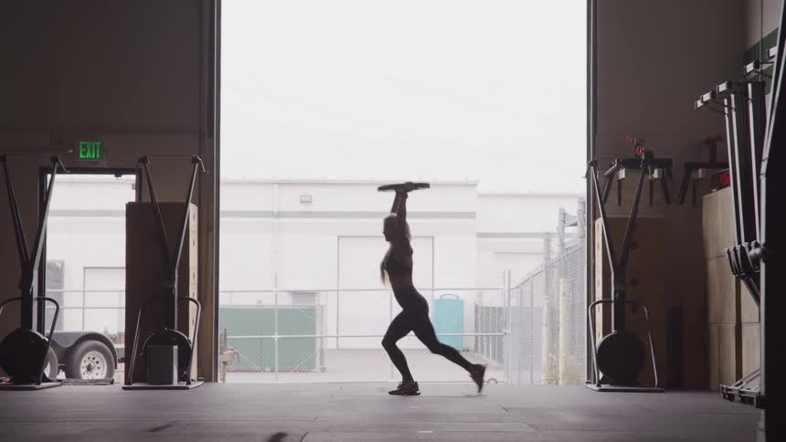 Woman in a gym doing lunges with a weight plate raised upwards