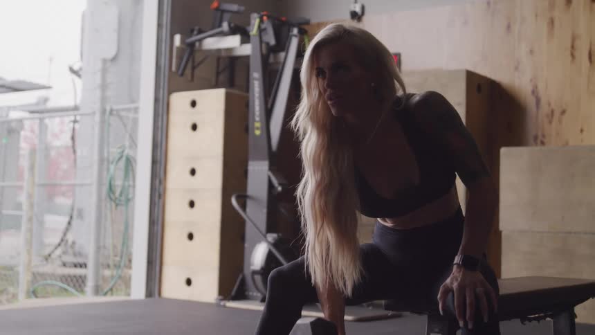 A woman is sitting on a bench lifting a dumbbell
