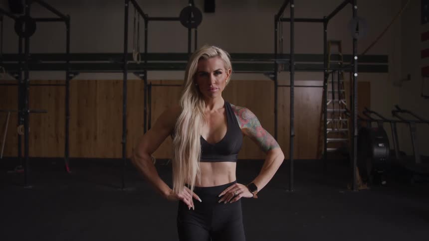 Blonde woman in sportswear with hands on hips is standing in a gym