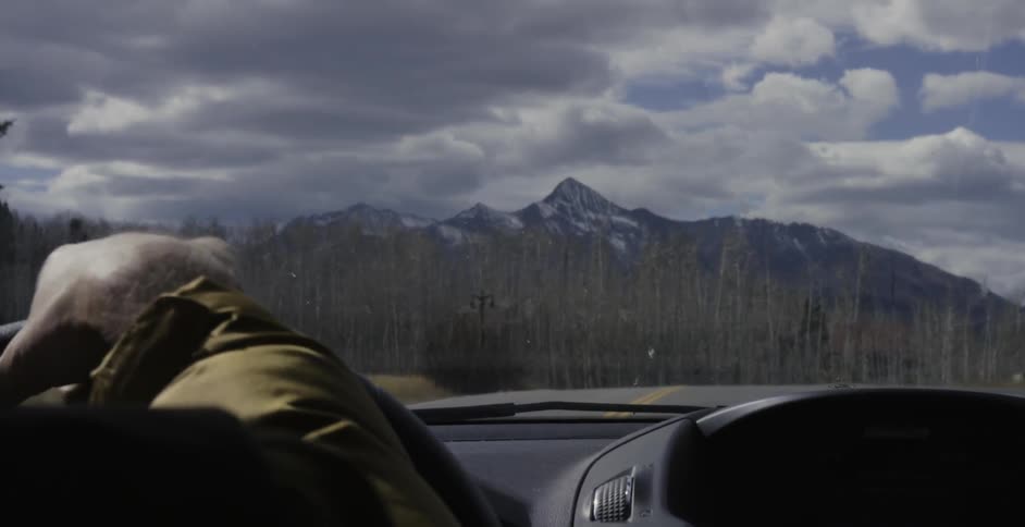 A man driving a vehicle towards the mountains with many clouds in the sky