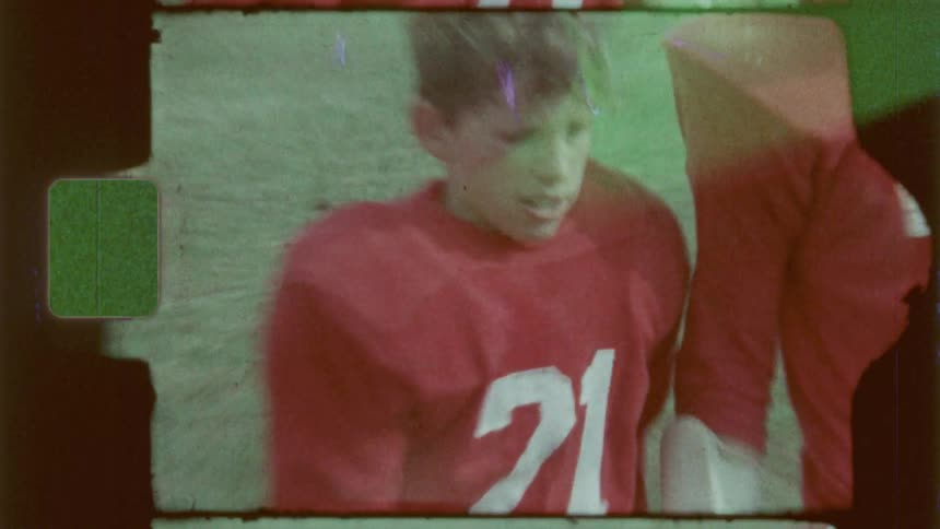 Teenage football players in red jerseys on a grassy field during a game captured on vintage film