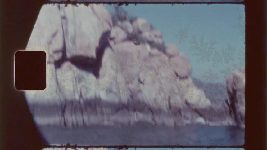 A vintage style shot captures a diver leaping from a rocky outcropping into the sea under a clear blue sky