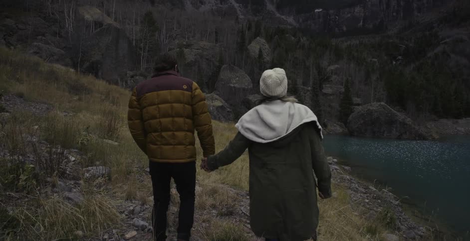 Couple holding hands as they walk the grassy bank of a lake