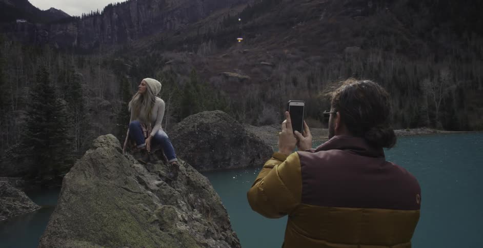 A girl is sitting on a large rock and a man is taking pictures of her