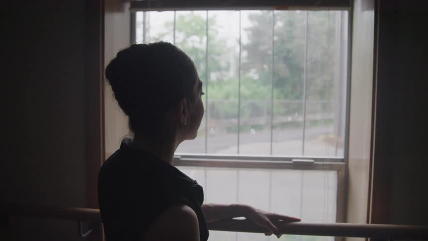 Ballerina in a ballroom looking out the window