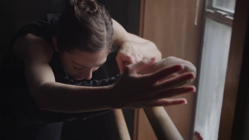 A ballet dancer is stretching in the studio