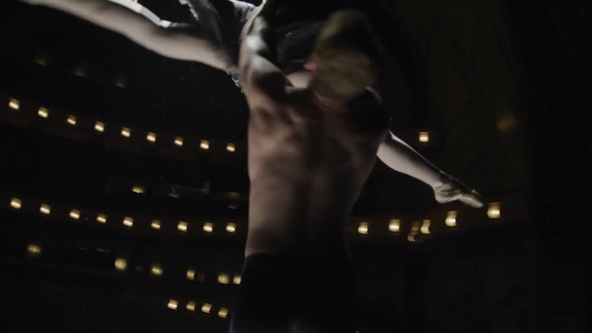 Two ballet dancers perform a lift on stage with one holding the other aloft in a poised graceful position