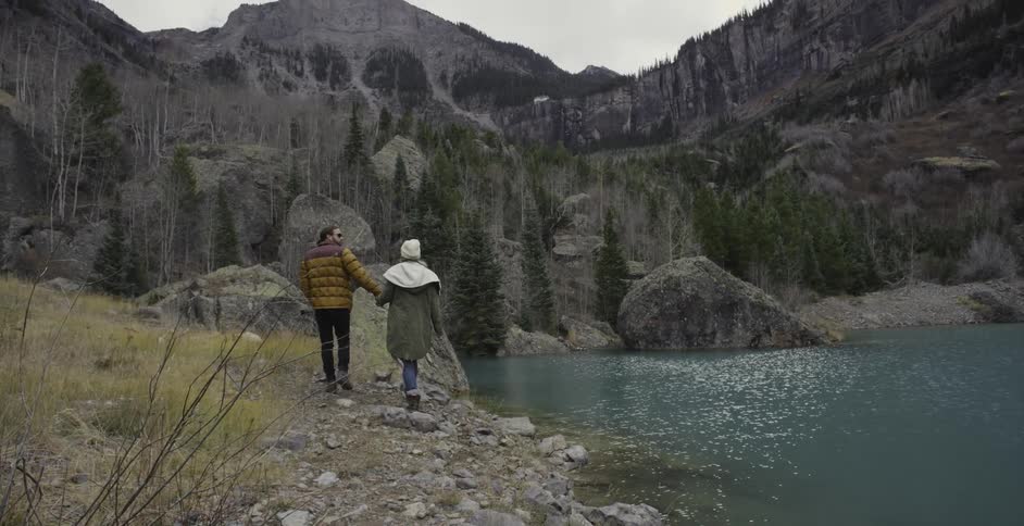 A couple of people walking next to some water and close to a large mountain