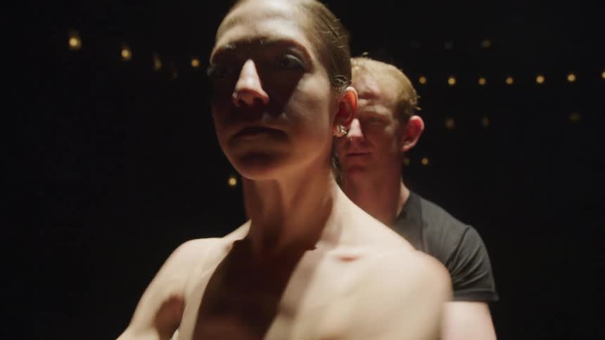 Man helps a ballerina spin while standing under a spotlight in a dark theater