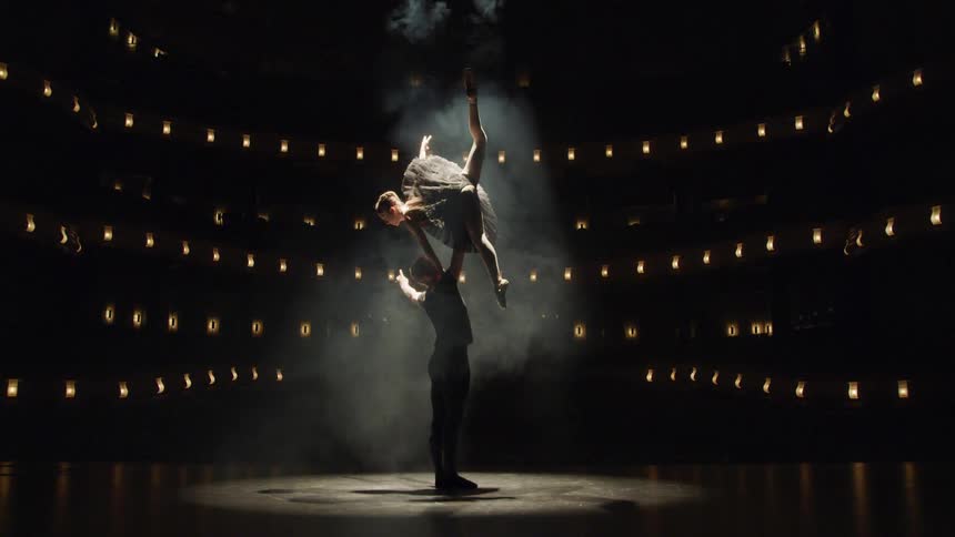 A male dancer lifts a ballerina in the air on stage