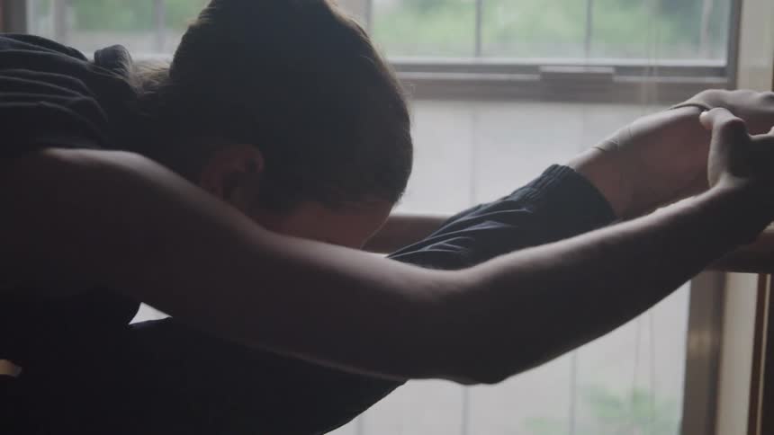 A woman leans forward while stretching in the ballet studio