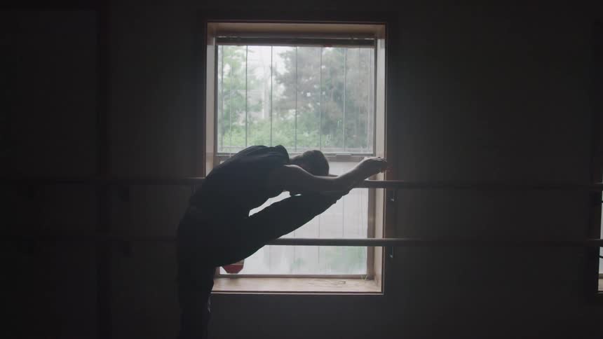 A woman is stretching in the ballet studio by the window